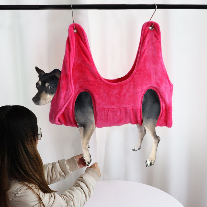 MATERA PET pink grooming hammock holding a small dog while the owner trims its front nails